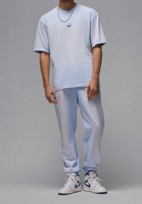 Světle modré bavlněné tričko s krátkým rukávem, doplněné o odpovídající tepláky. Obsahuje malý detail kapsy a bílé tenisky s modrými akcenty.