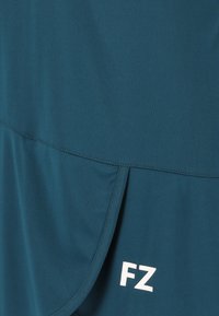 Aqua atletisk top med en glat tekstur, der har et lagdelt design og et hvidt "FZ" logo på den nederste front.