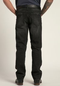 Jeans in denim nero con un design a gamba dritta, caratterizzati da cinque tasche e sottili dettagli strappati. Indossati con una cintura nera e scarpe.