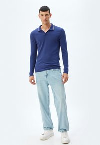 Mörkblå långärmad polo med krage som har vita ränder, matchad med ljusblå jeans och vita sneakers. Elegant och enkel design.