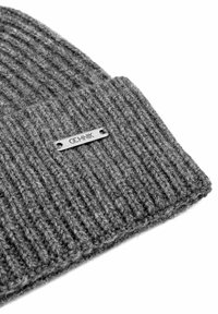 Zbliżenie szarej, prążkowanej czapki z dzianiny z małą, prostokątną metalową metką z napisem "COLNIK" przyszytą do mankietu.