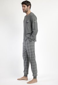 Camisa gris de manga larga con un diseño impreso en el pecho, combinada con pantalones de pijama grises de cuadros. Tejido suave y puños ajustados.