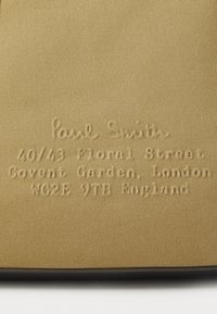Beige stof med prægede tekstdetaljer "Paul Smith" og en adresse: 40/43 Floral Street, Covent Garden, London, WC2E 9TB, England.