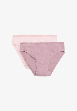 Mujer con bikini de estampado floral lavanda y un sujetador blanco, de pie frente a un fondo claro y liso.