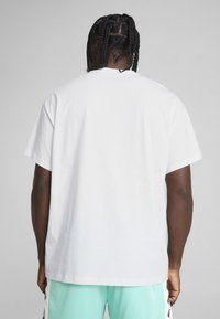 T-shirt en coton blanc avec une coupe décontractée, manches courtes et col rond. La vue arrière révèle une texture lisse, sans graphismes ni motifs.