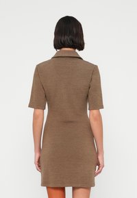 Καφέ φόρεμα με γιακά και κοντά μανίκια, κατασκευασμένο από πλεκτό ύφασμα, εφαρμοστή σιλουέτα και μήκος μέχρι το γόνατο. Απλή υφή χωρίς διακοσμήσεις.