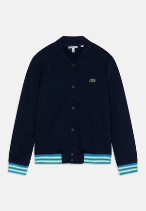 Navyblauwe katoenen cardigan met geribde kraag en manchetten. Heeft lichtblauwe en groene strepen aan de zoom en een klein groen logo op de borst.