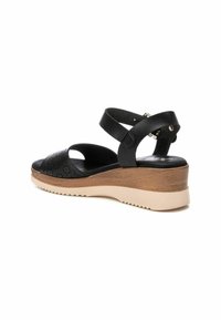 Sandalo in pelle nera con dettagli perforati, cinturini regolabili e suola in legno a zeppa. Presenta una suola in gomma beige texturizzata.