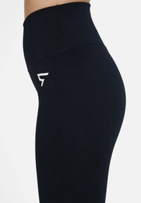 High-waisted black leggings with a textured fabric, featuring a white logo on the side and a smooth waistband for a snug fit.