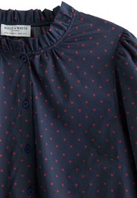 Námořnická halenka s volánkovým výstřihem, zdobená vzorem červených srdcí. Má knoflíkové zapínání vpředu a nafouklé rukávy.