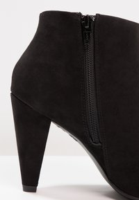 Mustat mokkanahkasaappaat nilkkapituisella varrella, joissa on korkea korko, sivuvetoketjuyksityiskohta ja sileä pinta, sekä tyylikäs muotoilu ja muotoiltu rakenne.