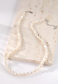 Collar de perlas con forma irregular, que presenta perlas blancas a crema, lisas y brillantes. Cierre de plata y detalle de cadena ajustable.