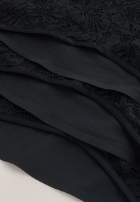 Couches de tissu noir alternant entre un matériau lisse et solide et une texture en dentelle florale, montrant les détails des bords et des coutures.