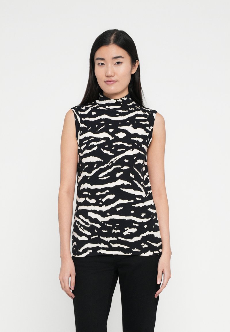 Fekete ujjatlan felső fehér zebra csíkos mintával, magas nyakkal és testhezálló fazonnal. Sima anyagból készült. Fekete nadrággal viselve.