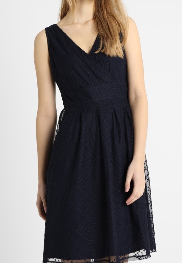 Robe bleu marine avec un décolleté en V et un design sans manches. Composée d'un tissu texturé avec un motif en losange et une bordure en dentelle le long de l'ourlet.