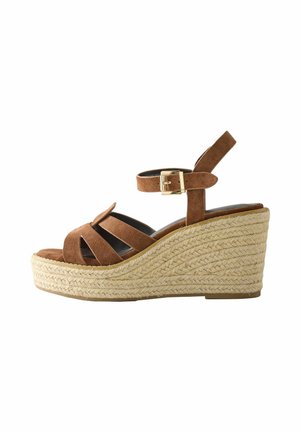 Braune Keilsandalette aus Wildleder mit geflochtenem Jute-Plateau, offenem Zehenbereich, Knöchelriemen und goldfarbener Schnalle auf weißem Hintergrund.
