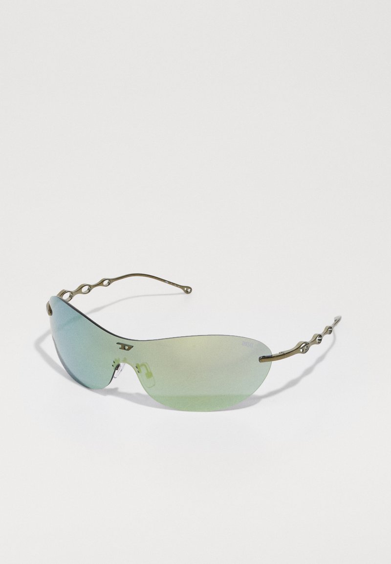 Lunettes de soleil avec des verres allongés teintés en vert. La monture en métal présente un design ondulé sur les branches avec de petits accents circulaires.
