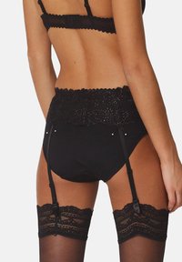 Schwarzes Wäscheset mit einem transparenten Spitzenband mit floralen Mustern, verstellbaren Trägern und Strumpfhaltern, die mit halterlosen Strümpfen verbunden sind.