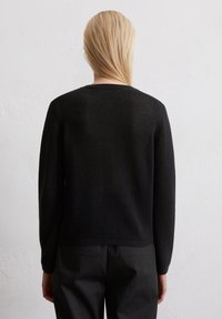 Schwarzer Pullover mit gerippter Textur, langen Ärmeln und Rundhalsausschnitt, kombiniert mit schwarzen Hosen. Der Hintergrund ist schlicht und hell.