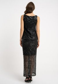 Czarna sukienka z cekinami, z dopasowanym gorsetem i przejrzystą spódnicą. Materiał jest błyszczący o gładkiej fakturze. Tył posiada subtelny zaokrąglony dekolt.