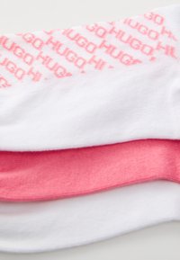 Cotton socks in white and light pink, featuring a repeated logo pattern in pink along the cuff and ribbed texture for added grip.