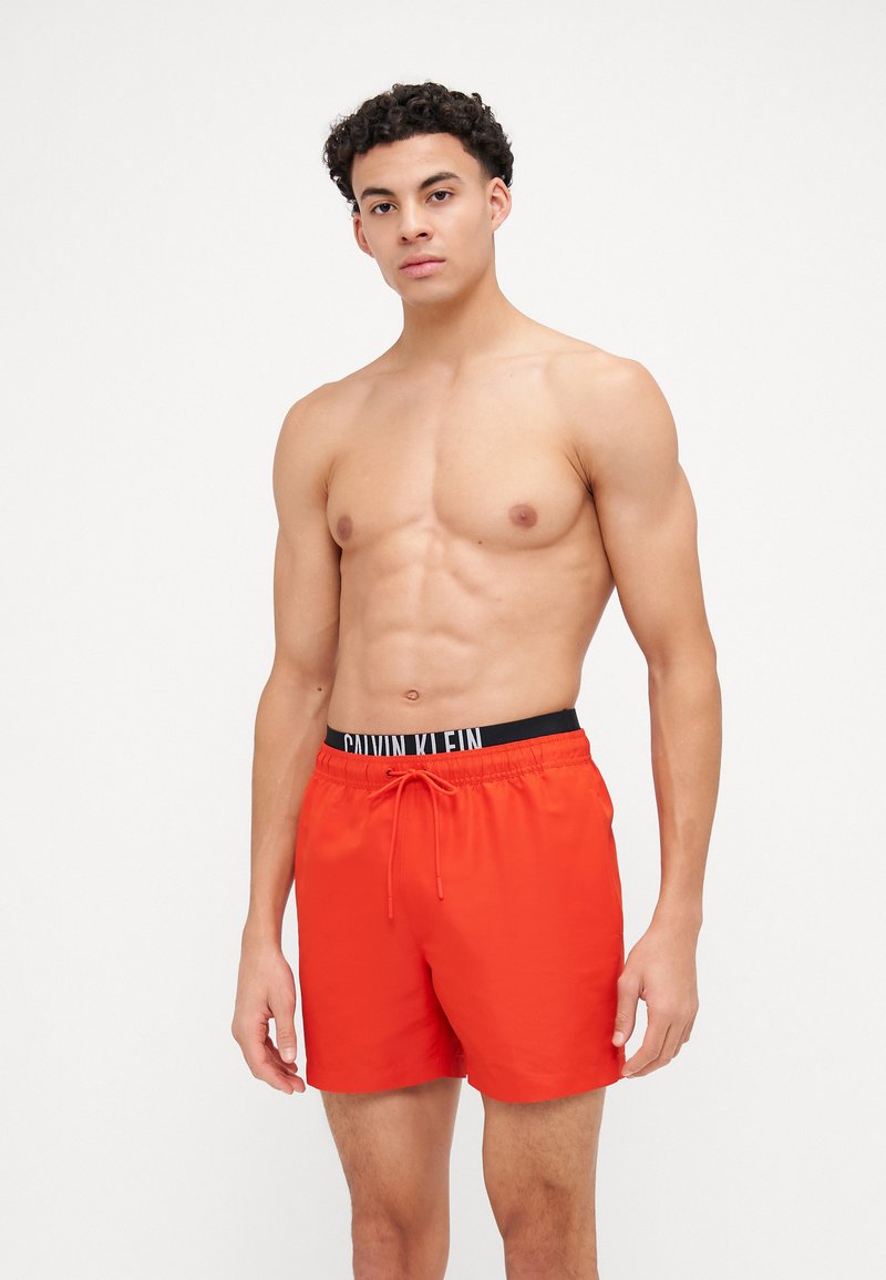 Shorts de bain rouges avec une taille élastique noire arborant le logo "CALVIN KLEIN", fermeture à cordon de serrage et tissu lisse et léger.
