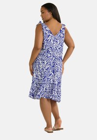 Blå och vit mönstrad klänning med v-rygg, justerbara knytband och en lager-på-lager, utsvängd kjoldesign. Lättviktigt material, avslappnad passform.