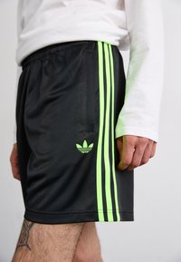 Fekete sportnadrág három függőleges neon zöld csíkkal és egy kis zöld Adidas logóval a bal oldalon. Könnyű anyag, rugalmas derékpánt.