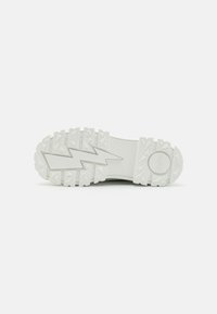 Witte rubberen sneakerzool met een zigzagpatroon, voorzien van een gestructureerde grip en een glad middelste deel, met een gebrandmerkte cirkelvormige logo aan de zijkant.