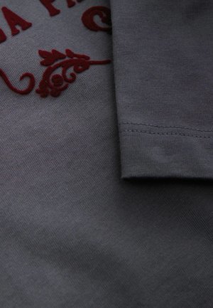 Gray cotton fabric with a smooth texture, featuring burgundy embroidered floral details and a folded sleeve, showcasing clean stitching.