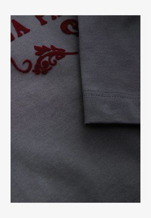 Hallhalli puuvillakangas sileda tekstuuriga, millel on burgaunia tikitud lillemotiivid ja volditud varrukas, näidates puhtaid õmblusi.