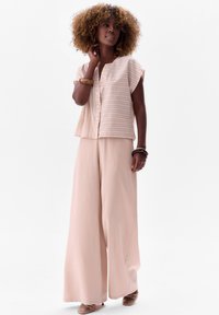 Jasnoróżowa bluzka w paski z krótkim rękawem i guzikiem z przodu, w połączeniu z szerokimi jasnoróżowymi spodniami, gładki materiał, luźny krój.