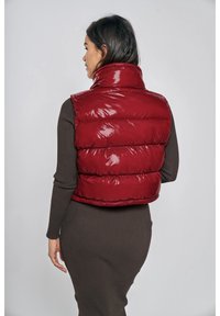Czerwona puchowa kamizelka o błyszczącym wykończeniu, z wysokim kołnierzem i poziomym pikowaniem, noszona na dopasowanej brązowej sukience.