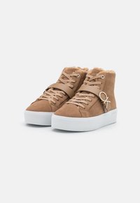 Sneaker high-top in suede color sabbia con suole in gomma bianca, dotate di una fodera morbida, una fascia beige a livello dell'arco del piede e un logo circolare decorativo.