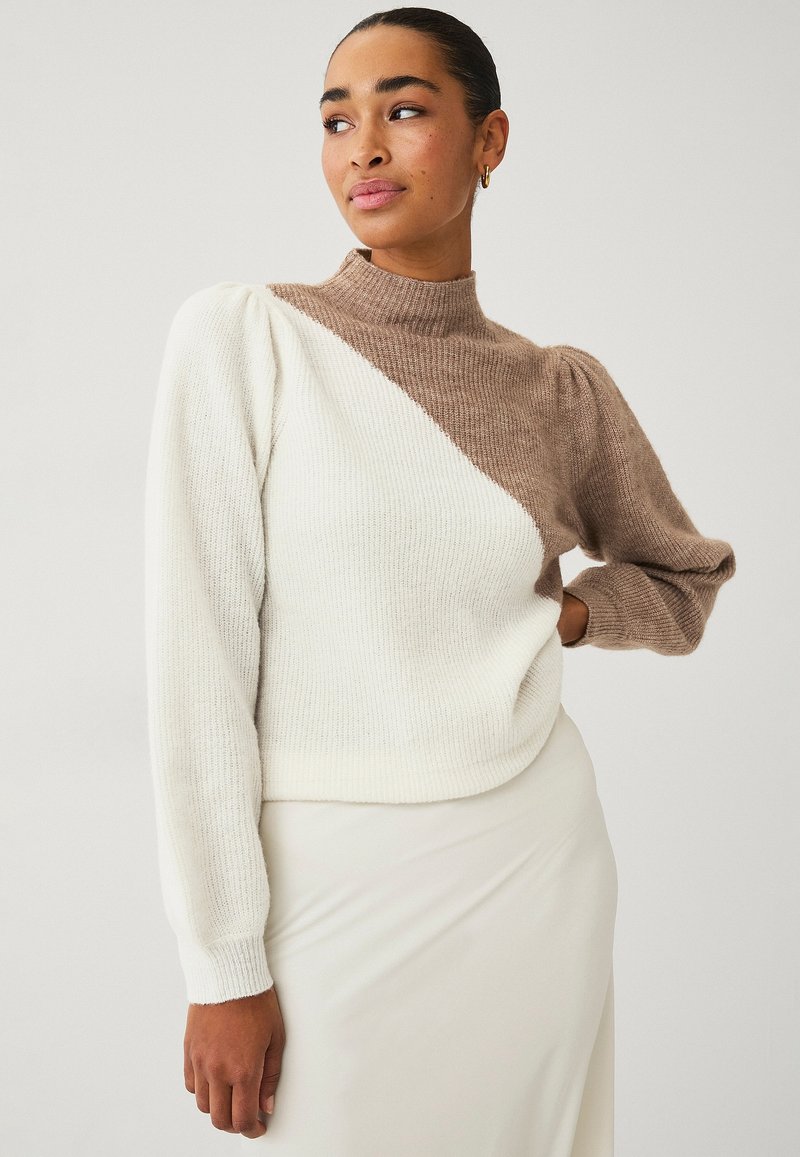 Maglione lavorato a maglia con colletto alto, caratterizzato da un design a blocchi di colore diagonali in crema e marrone. Texture morbida, maniche lunghe con dettaglio a palloncino.