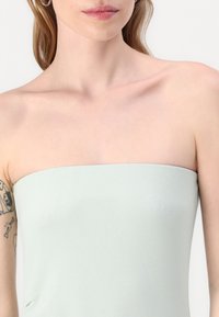 Šviesiai žalia, be petnešėlių palaidinė su glotnia, tekstūruota medžiaga. Yra tiesi iškirptė ir prigludusi forma, akcentuojanti minimalistinę siluetą.
