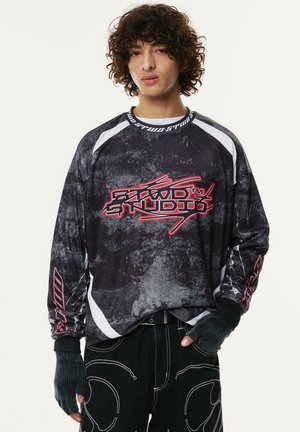 Fekete pulóver texturált, absztrakt mintával, fehér kiemelésekkel és piros grafikai logóval. Hosszú ujjú, ujjak nélküli kesztyűszerű textúrával rendelkezik.