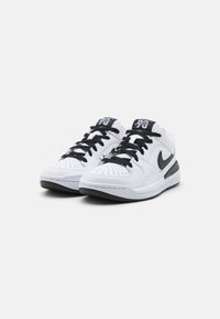 Fekete fűzővel ellátott fehér és fekete Nike Air Jordan sportcipők egy sima fehér háttéren.
