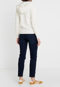 Sudadera con capucha gris claro y un bolsillo tipo canguro, combinada con unos jeans ajustados azul oscuro y zapatillas de ante color beige con rayas blancas.