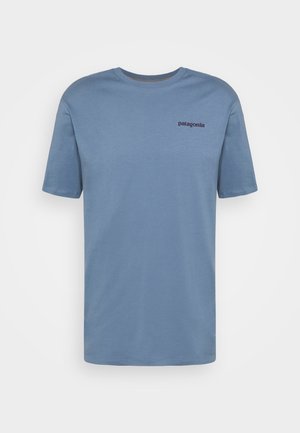 Camiseta de algodón de manga corta en azul claro, con un escote redondo y un pequeño logo oscuro en la parte superior izquierda del pecho.