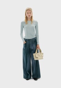 Top de manga larga azul claro, pantalones de mezclilla de pierna ancha de color azul oscuro y un pequeño bolso de crema. Tejido suave con un ajuste casual. Zapatos negros.