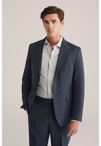 Blazer blu navy con un motivo testurizzato, chiusura a un bottone, rever a punta e una camicia chiara sotto. Vestibilità sagomata.