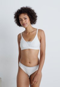 White lingerie set featuring a bralette with adjustable straps and a geometric band, paired with matching briefs. Smooth texture and minimalist design.
