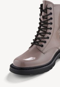 Bottine brillante taupe à lacets, avec semelle épaisse en caoutchouc noir et œillets et lacets noirs, présentée de face et de côté.