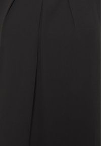 Abito nero realizzato in un tessuto liscio, con un delicato dettaglio a pieghe che crea una superficie elegante e piatta senza motivi o hardware visibili.