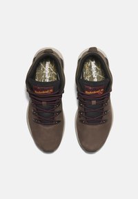 Zapatos de exterior marrones con parte superior de cuero suave, acentos negros, cordones burdeos y una plantilla con patrón. Presentan un collar acolchado.