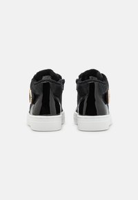 Zapatillas altas negras con acabado de charol brillante, tejido texturizado, suela de goma blanca y detalle en dorado en el talón.