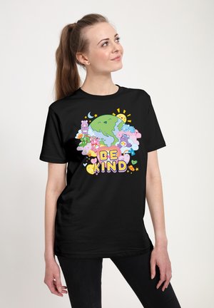 Vrouw draagt een zwart shirt met kleurrijke cartoon van de aarde, zon, wolken, teddyberen en de tekst "Wees vriendelijk" aan de voorkant.