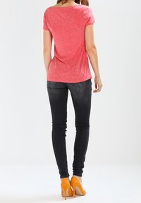 Camiseta roja de manga corta, corte relajado, combinada con jeans negros ajustados y zapatos de tacón altos anaranjados. Diseño liso sin patrones visibles.