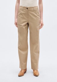 Beežid puuvillased püksid sirge lõikega, esitaskud, ühe nupuga kinnis, peene tekstuuriga, kombineeritud pruunide nahast pahkluu-saabastega.